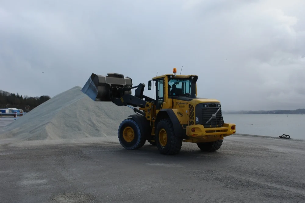 Gummiged ved bunke af grus på havnen